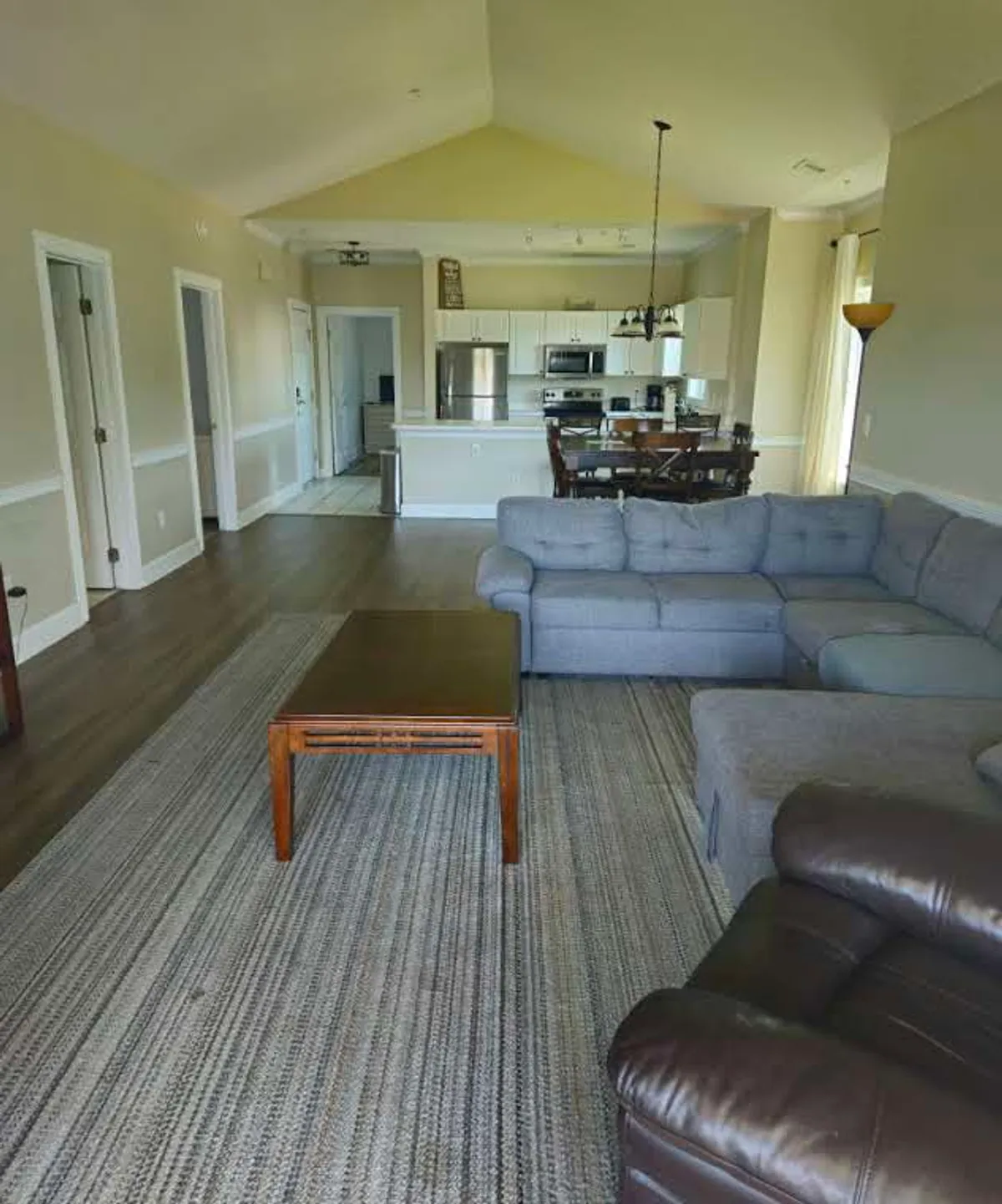 This image showcases the condo's open-concept living area, featuring a comfortable sofa, coffee table, dining area, and a view into the kitchen. The layout suggests a spacious and inviting environment where families or groups can gather, unwind after a day exploring local attractions, or plan the next day's adventures.