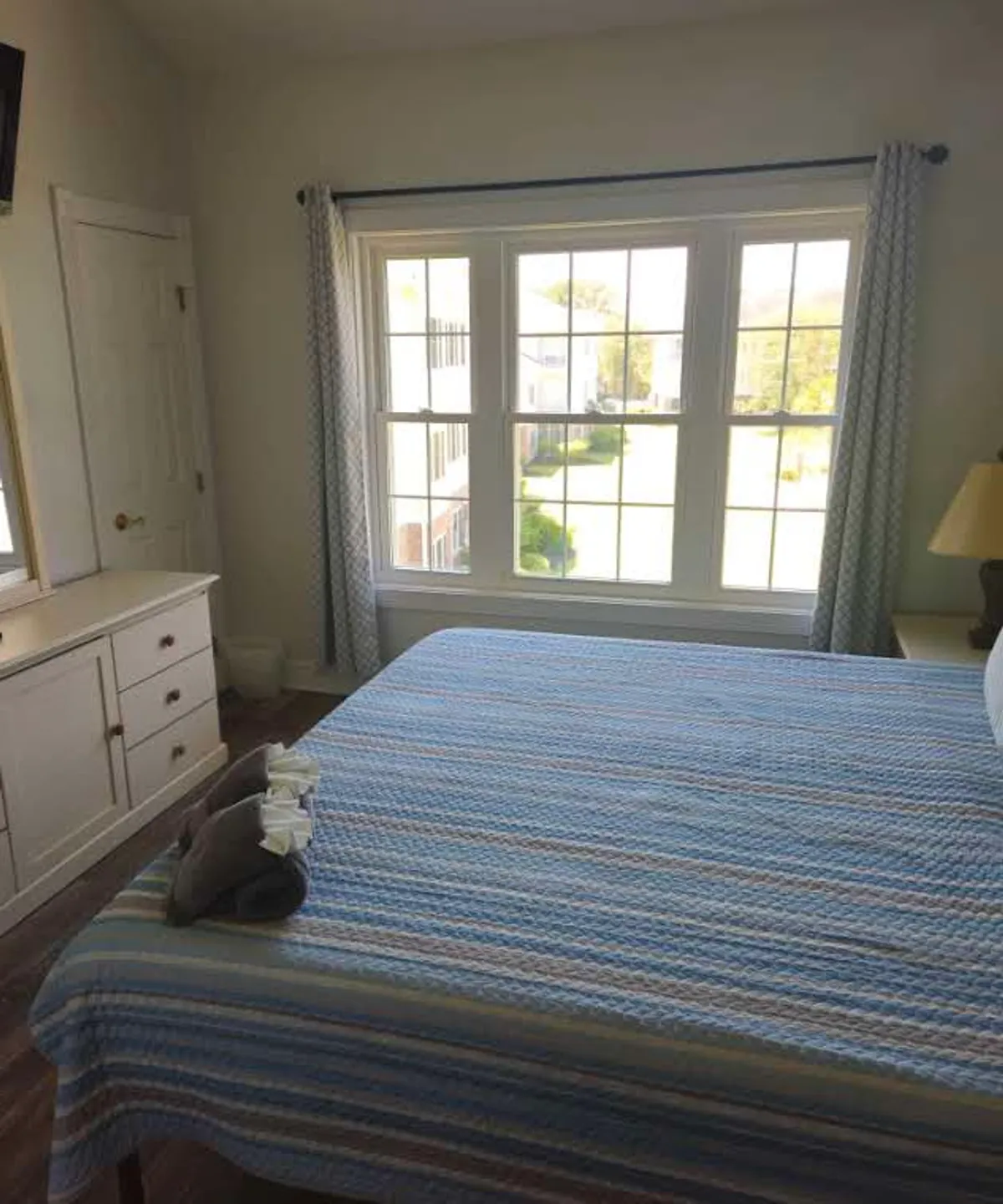 This image highlights a peaceful bedroom with a bed adorned in a striped blanket, a large window letting in natural light, a dresser, and a cozy lamp. The setting emphasizes relaxation and comfort, while the window view subtly hints at the condo's elevated placement and serene golf course surroundings.