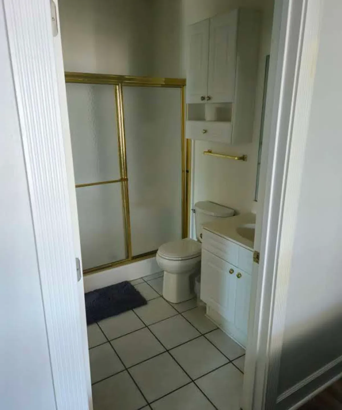 A sparkling clean bathroom featuring a glass-door shower with gold trim, white cabinetry, a toilet, and a sink. The space feels refreshed and modern, ideal for morning and evening routines.