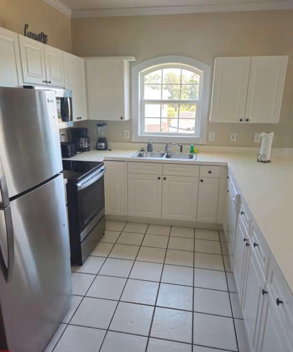 This image features a spacious and inviting kitchen with stainless steel appliances, white cabinetry, and a window above the sink that lets in natural light. The warm and welcoming atmosphere suggests it's an ideal hub for meal prep, cooking together, or sharing stories over food.